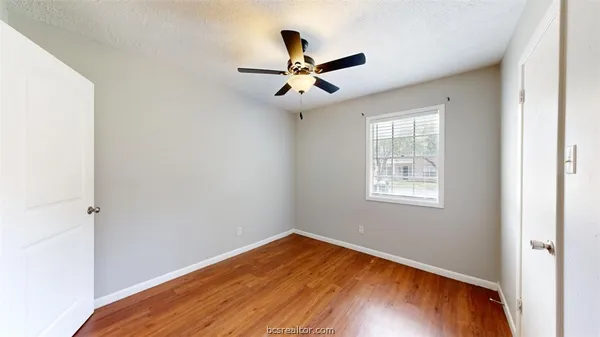 an empty room with wooden floor ceiling fan and windows