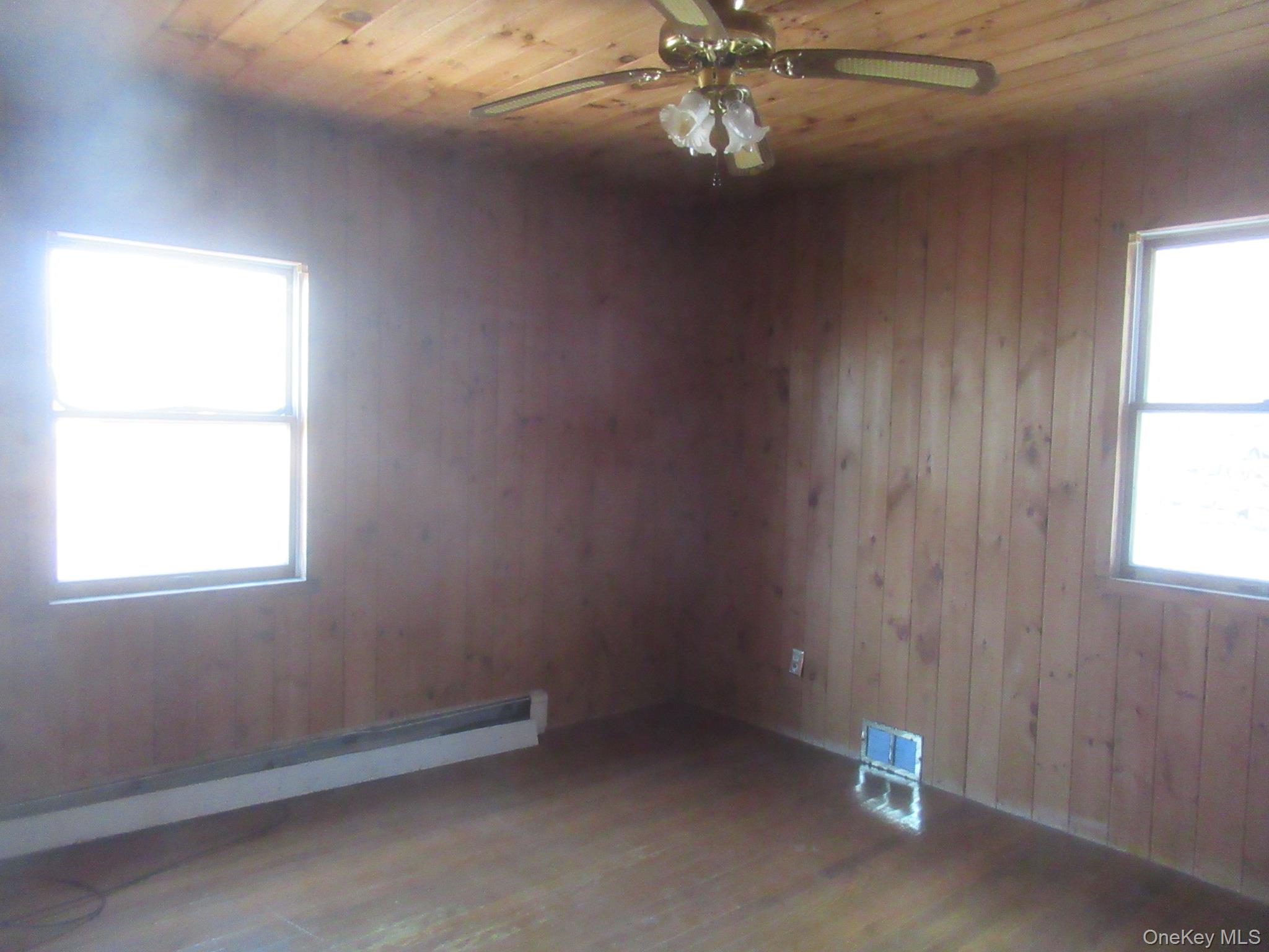270 Bucks Hollow Road Mahopac, NY 10541 - Photo 10 of 11 Empty room featuring wooden ceiling, wood walls, a ceiling fan, wood finished floors, and a baseboard heating unit