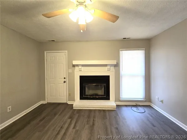 an empty room with wooden floor a chandelier fan and a fireplace