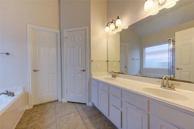 a spacious bathroom with a double vanity sink a large mirror and a bathtub
