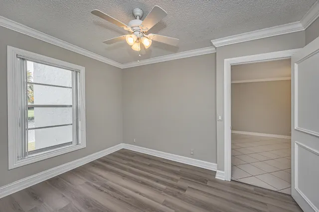 an empty room with wooden floor chandelier fan and windows