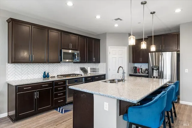 a kitchen with stainless steel appliances granite countertop a sink a stove a refrigerator cabinets and wooden floor