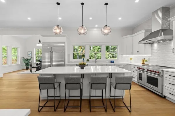 a kitchen with stainless steel appliances granite countertop a stove top oven a refrigerator a kitchen island a dining table and chairs with wooden floor