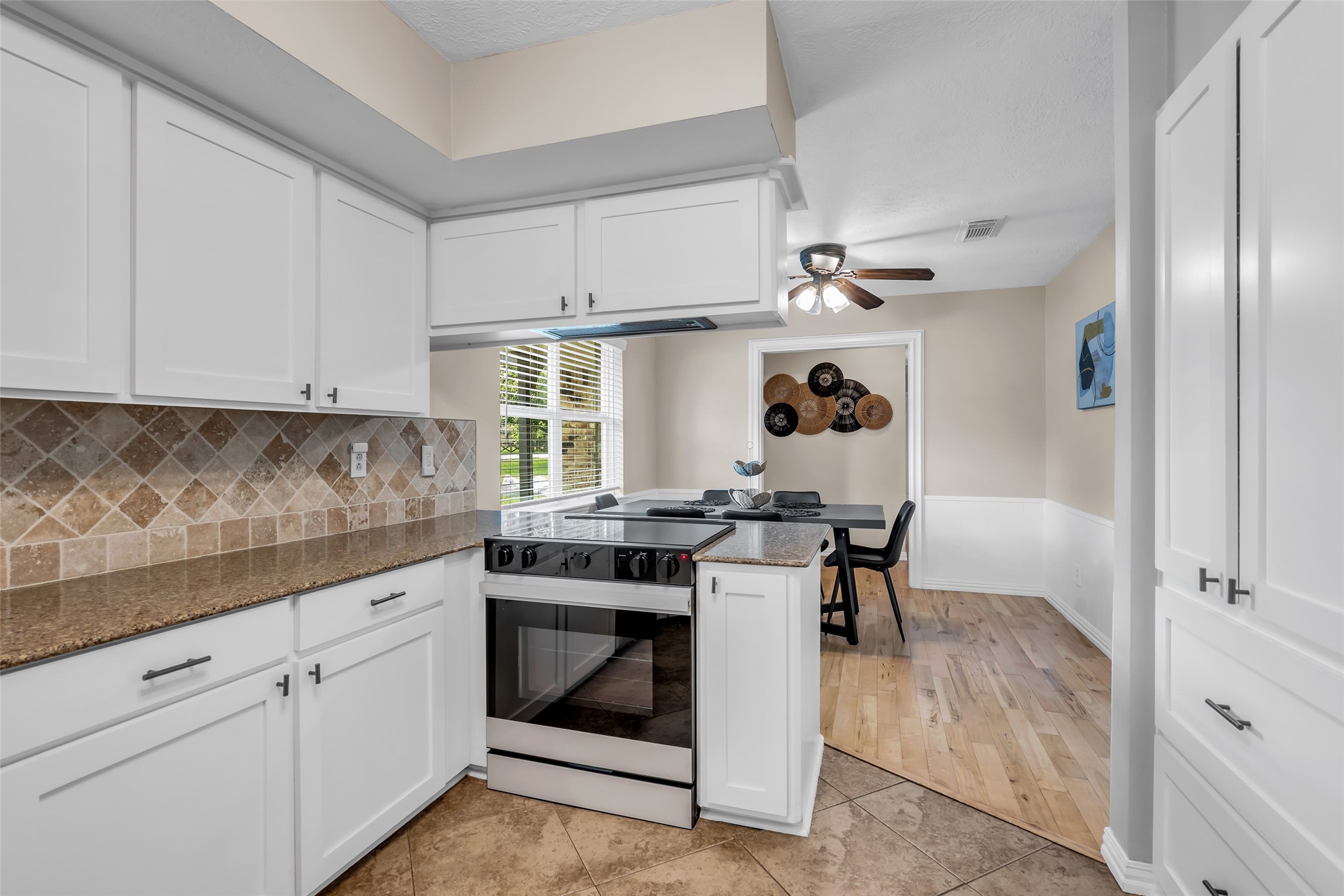 22502 Fields Lane Spring, TX 77389 - Photo 17 of 39 Open concept kitchen with white cabinetry, stone backsplash, and granite countertops. It opens to a dining area with hardwood floors and a ceiling fan, creating a bright and inviting space.