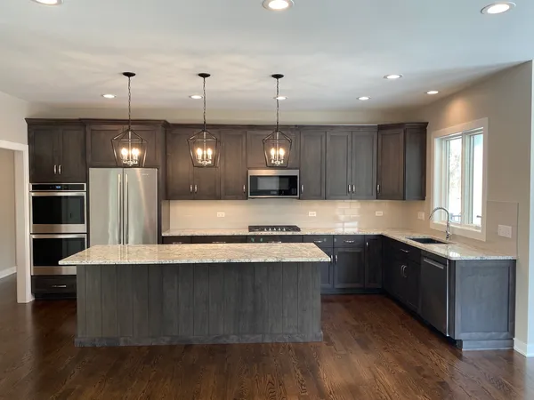 a large kitchen with stainless steel appliances kitchen island granite countertop a stove a refrigerator a sink dishwasher a oven and a dining table with wooden floor
