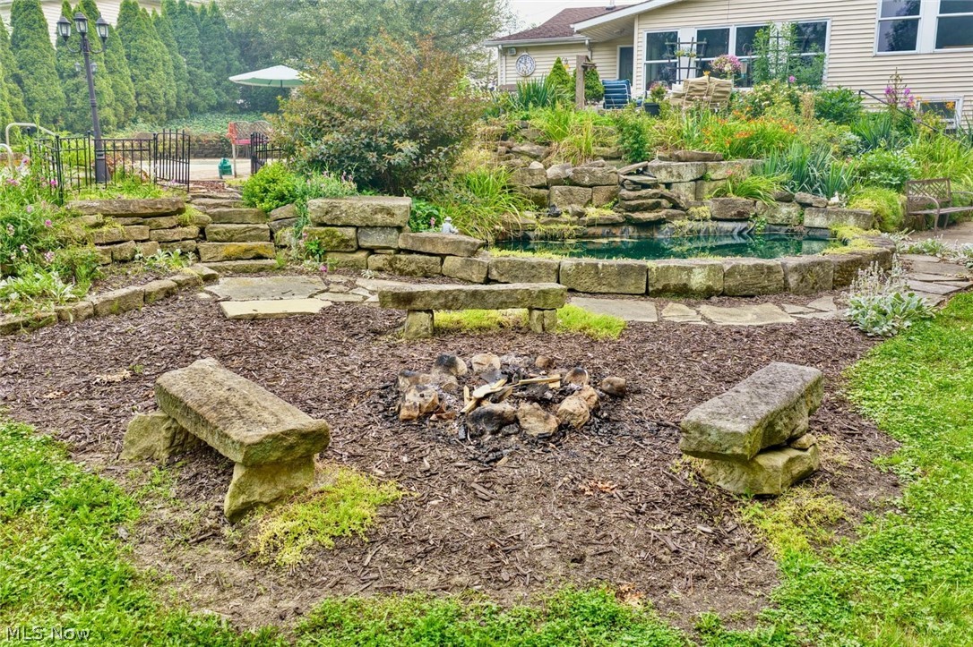 6549 Waterloo Road Atwater, OH 44201 - Photo 4 of 49 Terraced backyard featuring a stone-lined fire pit, natural stone benches, and a multi-level rock garden with a pond