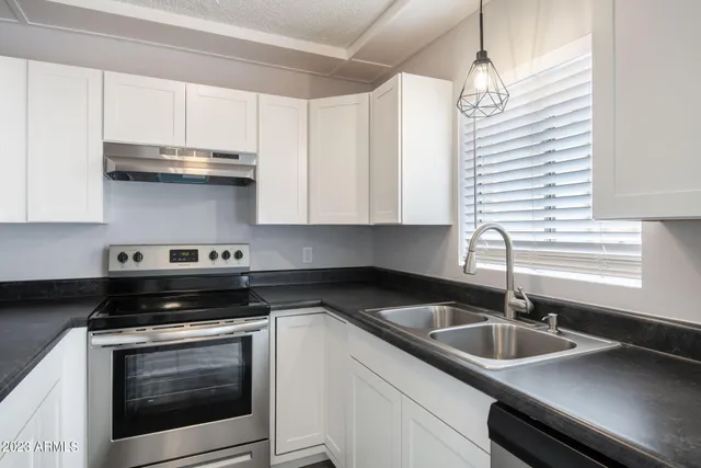 a white kitchen with granite countertop a sink a stove and cabinets