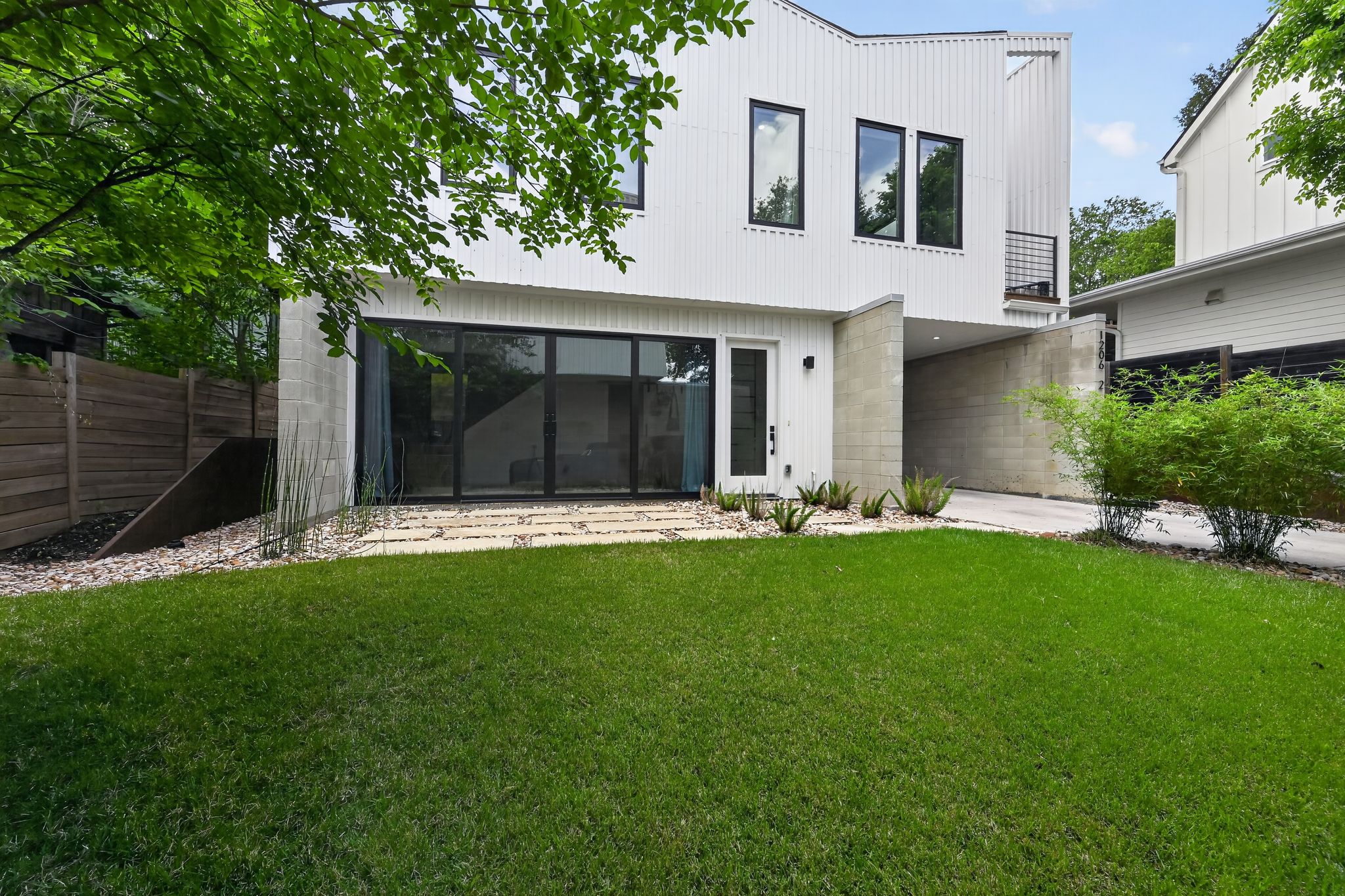 1206 Luna Street, Unit 2 Austin, TX 78721 - Photo 2 of 30 The property features a modern white exterior with black-framed windows, a well-maintained lawn, and a fenced side yard