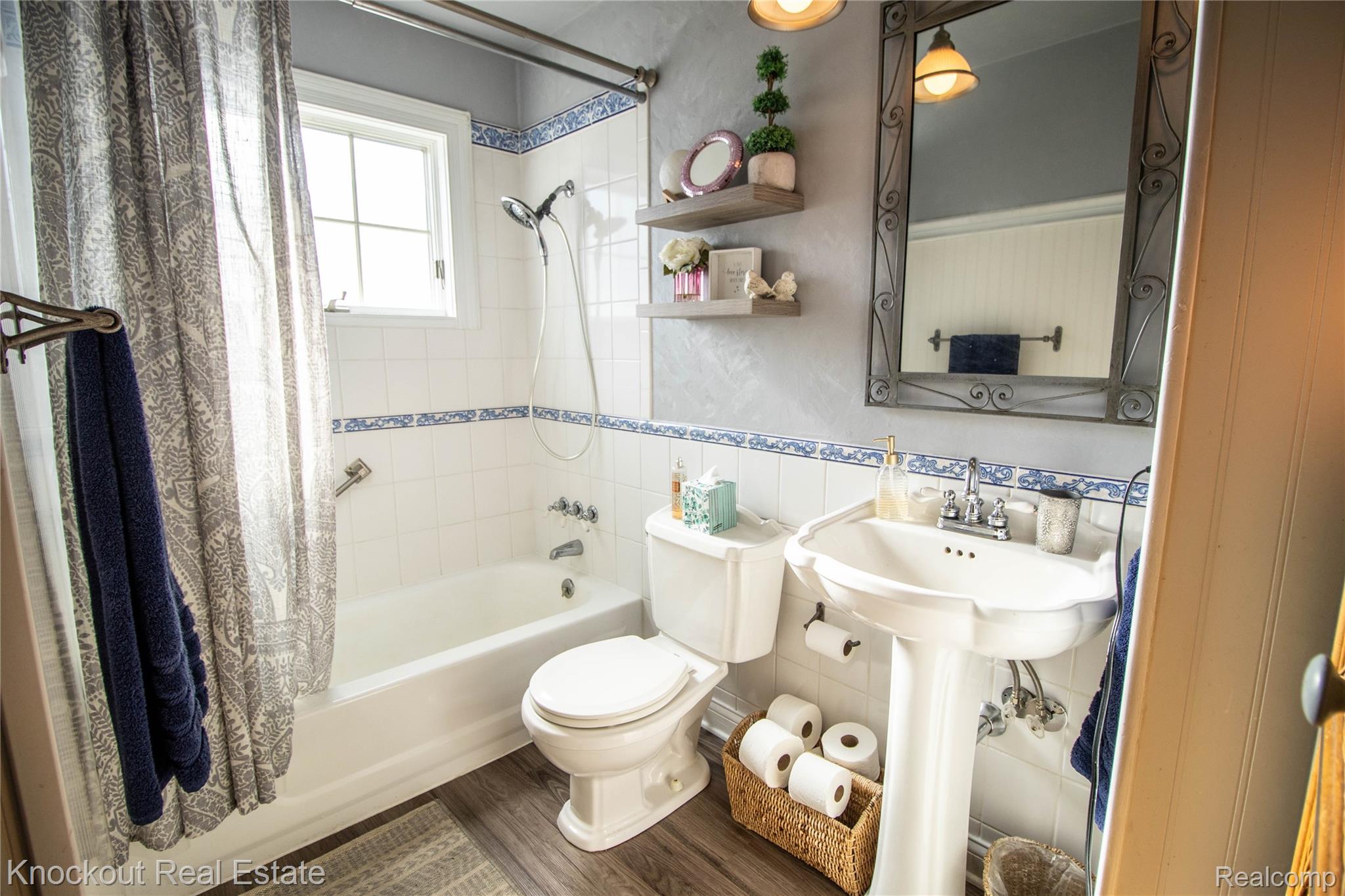 14720 Lincoln Road Chesaning, MI 48616 - Photo 32 of 60 White subway tile walls with decorative blue trim, pedestal sink, wall-mounted mirror, wood-finish flooring, and window with privacy glass