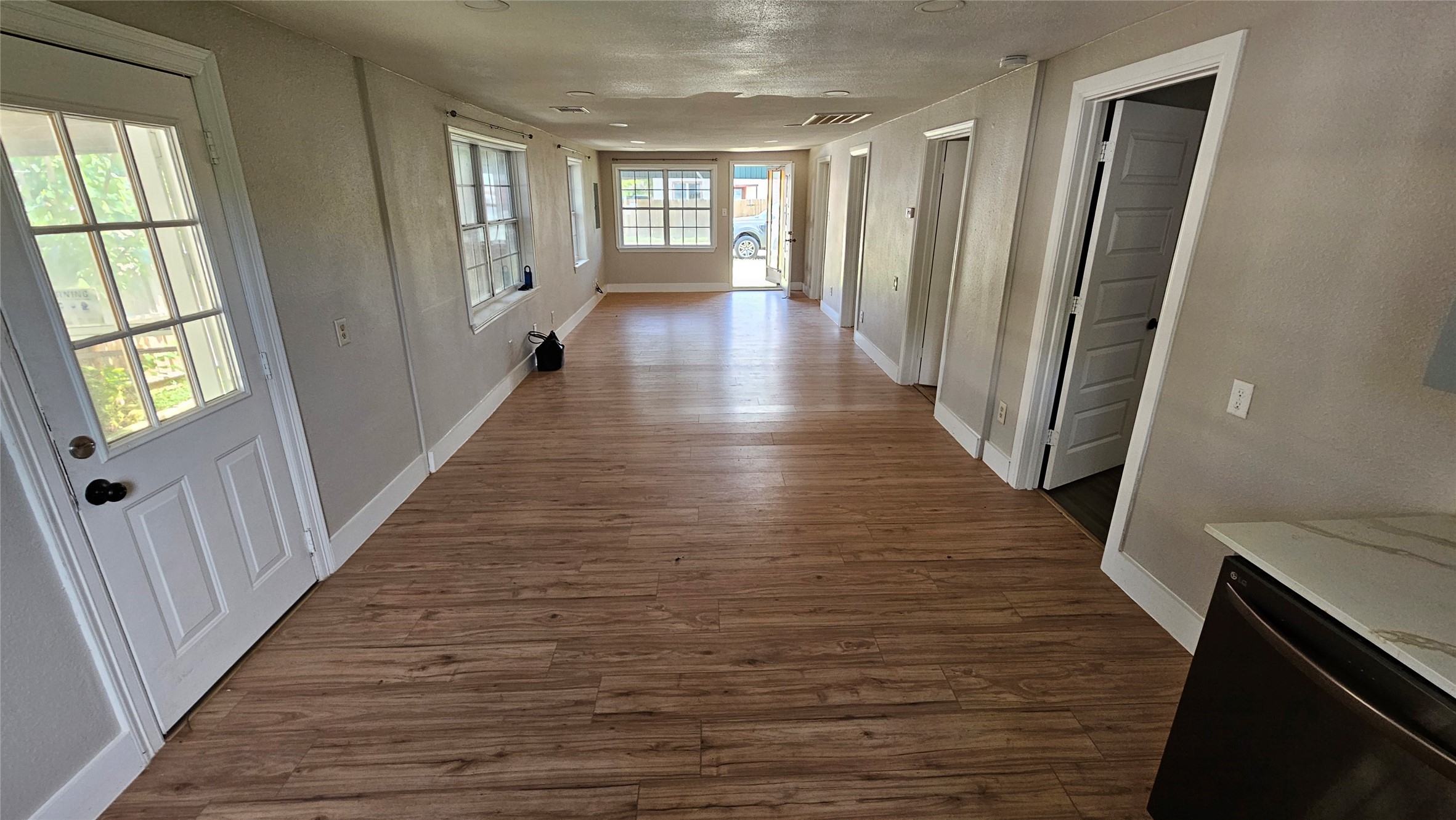 2415 Perry Street Baytown, TX 77521 - Photo 8 of 23 This photo shows a long, bright living space with wood-look flooring, leading to a sunlit room with large windows. There are several doors along the right side and a glass-paneled door on the left, providing access to the outdoors. Clean and inviting space.