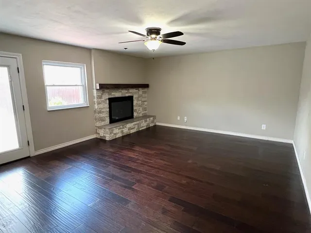 a view of an empty room with wooden floor fireplace and a window