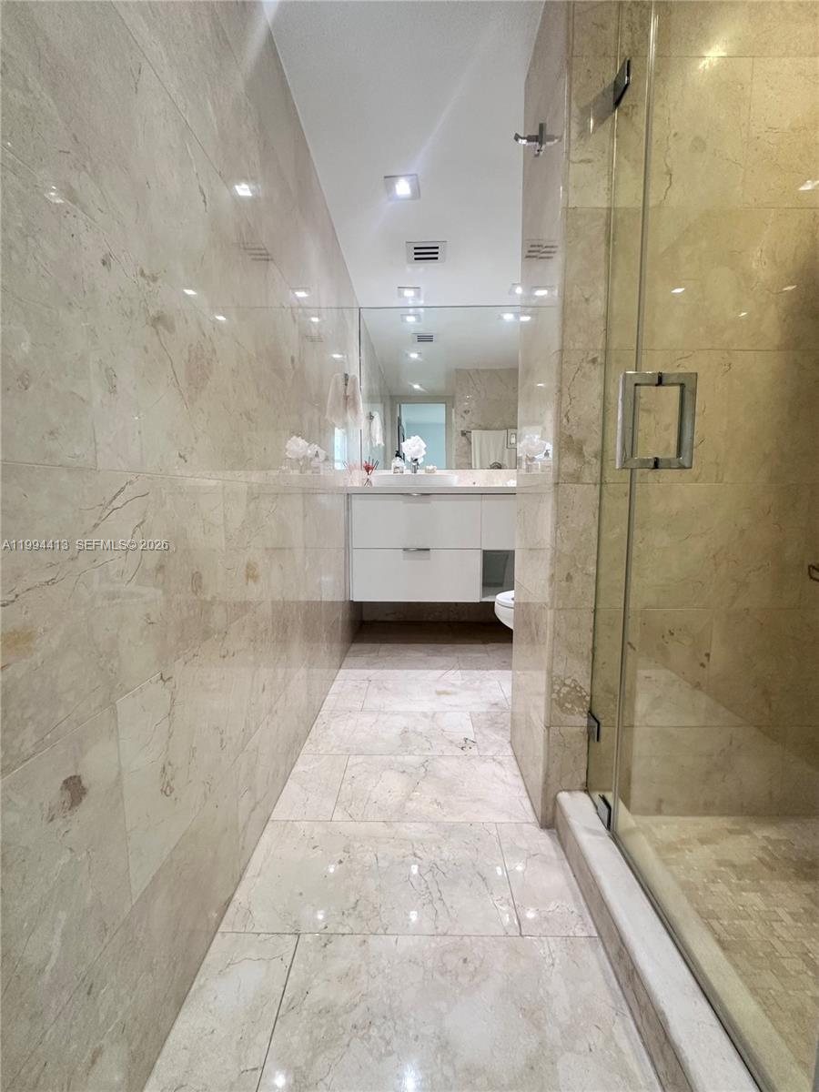 9225 Collins Avenue, Unit 1111 Surfside, FL 33154 - Photo 19 of 54 a bathroom with a glass door shower a sink and a mirror