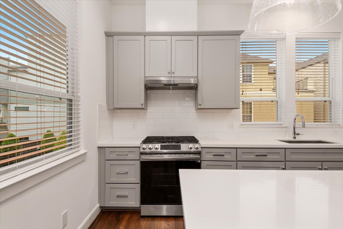 2777 Clinton Drive Houston, TX 77020 - Photo 13 of 37 This modern kitchen features sleek gray cabinetry, a stainless steel gas range with a hood, and a bright, airy atmosphere enhanced by large windows and white countertops.