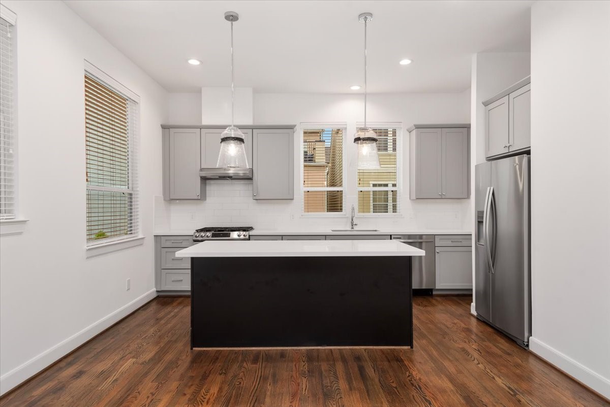 2777 Clinton Drive Houston, TX 77020 - Photo 5 of 37 This modern kitchen features sleek gray cabinetry, stainless steel appliances, and a central island with pendant lighting. It boasts hardwood floors, white subway tile backsplash, and ample natural light from multiple windows.