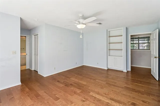 an empty room with wooden floor closet and windows