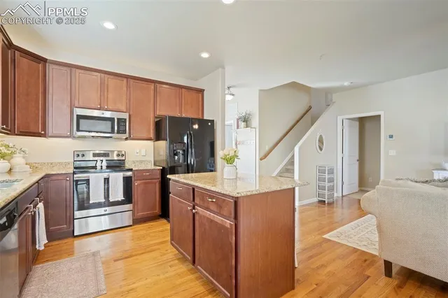a kitchen with stainless steel appliances granite countertop a refrigerator a stove top oven a sink dishwasher and wooden cabinets with wooden floor