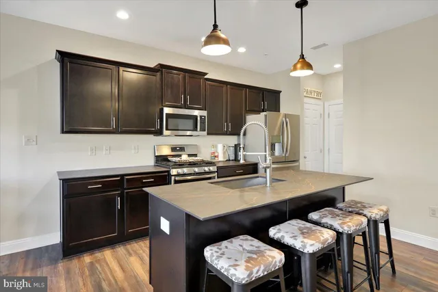 a kitchen with a refrigerator a stove a sink dishwasher a dining table and chairs with wooden floor