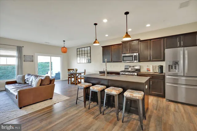 a kitchen with stainless steel appliances granite countertop a refrigerator a stove a sink a dining table and chairs with wooden floor