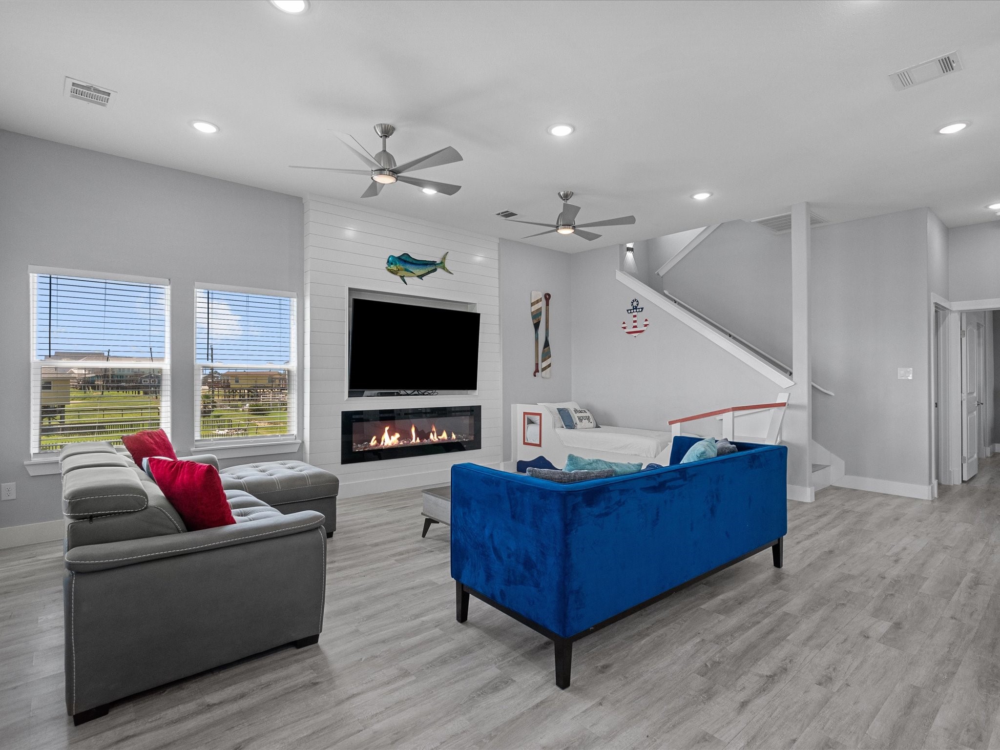718 Beach Drive Surfside Beach, TX 77541 - Photo 20 of 49 Discover a bright and inviting open-concept living space featuring a modern kitchen with white cabinetry and a striking blue tile backsplash. Enjoy a cozy seating area with colorful couches and charming nautical decor, all enhanced by abundant lighting and large windows.