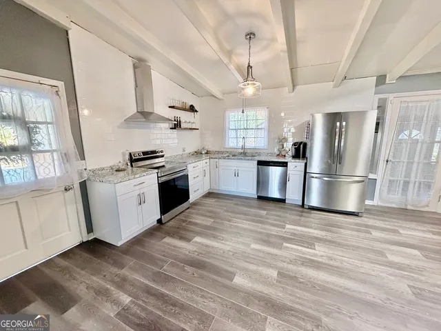 a kitchen with stainless steel appliances granite countertop a refrigerator a stove a sink dishwasher and white cabinets with wooden floor