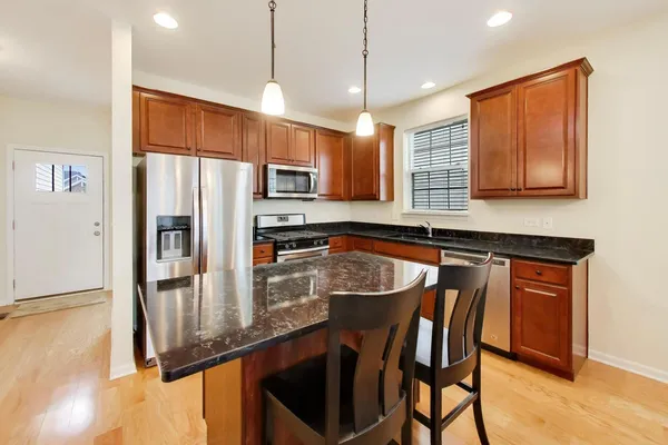 a kitchen with stainless steel appliances granite countertop a refrigerator a stove a sink a dining table and chairs with wooden floor