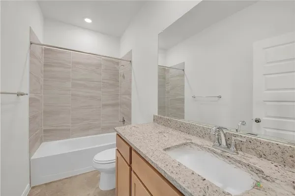 a bathroom with a granite countertop bathtub shower sink vanity mirror and toilet