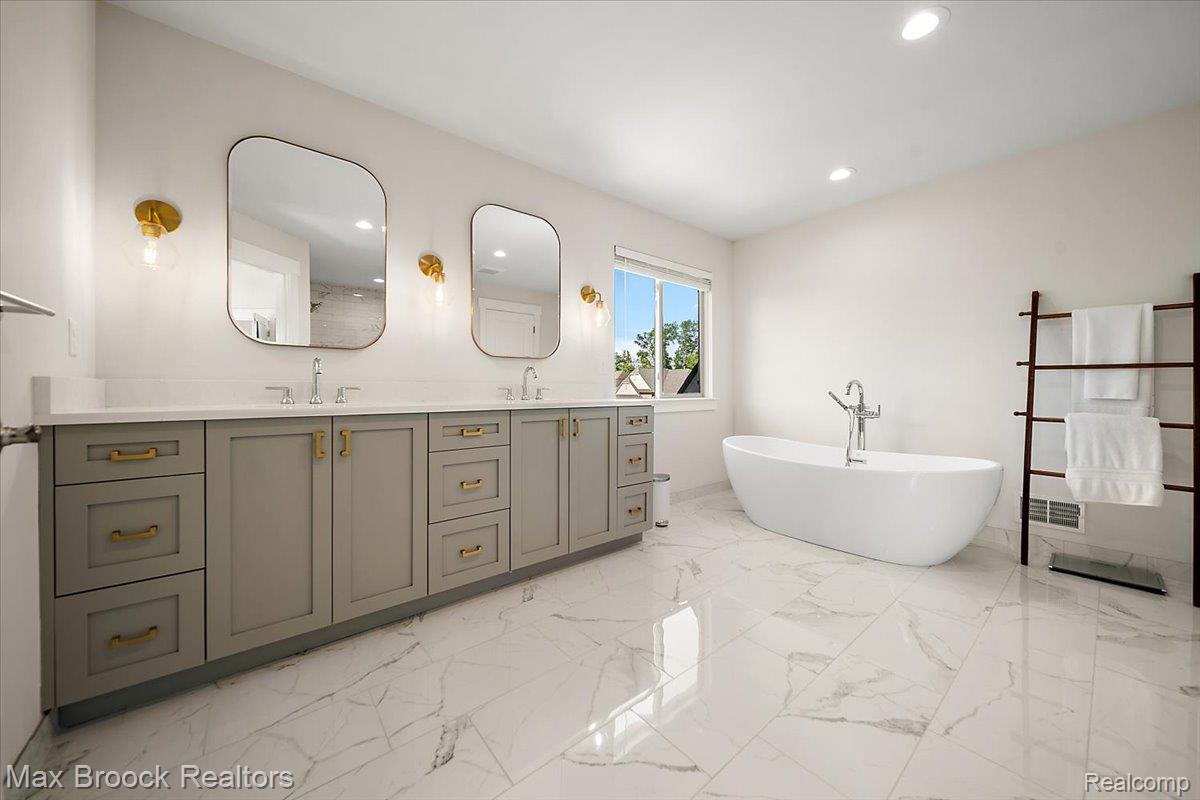 1942 Nottingham Drive Rochester, MI 48307 - Photo 51 of 97 Spacious bath featuring a freestanding soaking tub, dual vanity with quartz countertops, custom cabinetry, and large format marble-look tile flooring