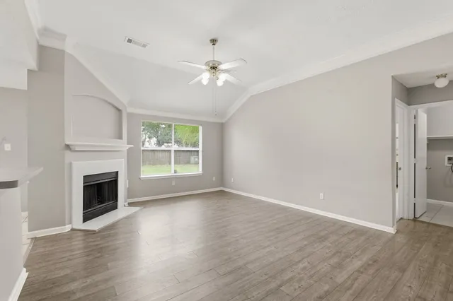 a view of an empty room with wooden floor fireplace and a window