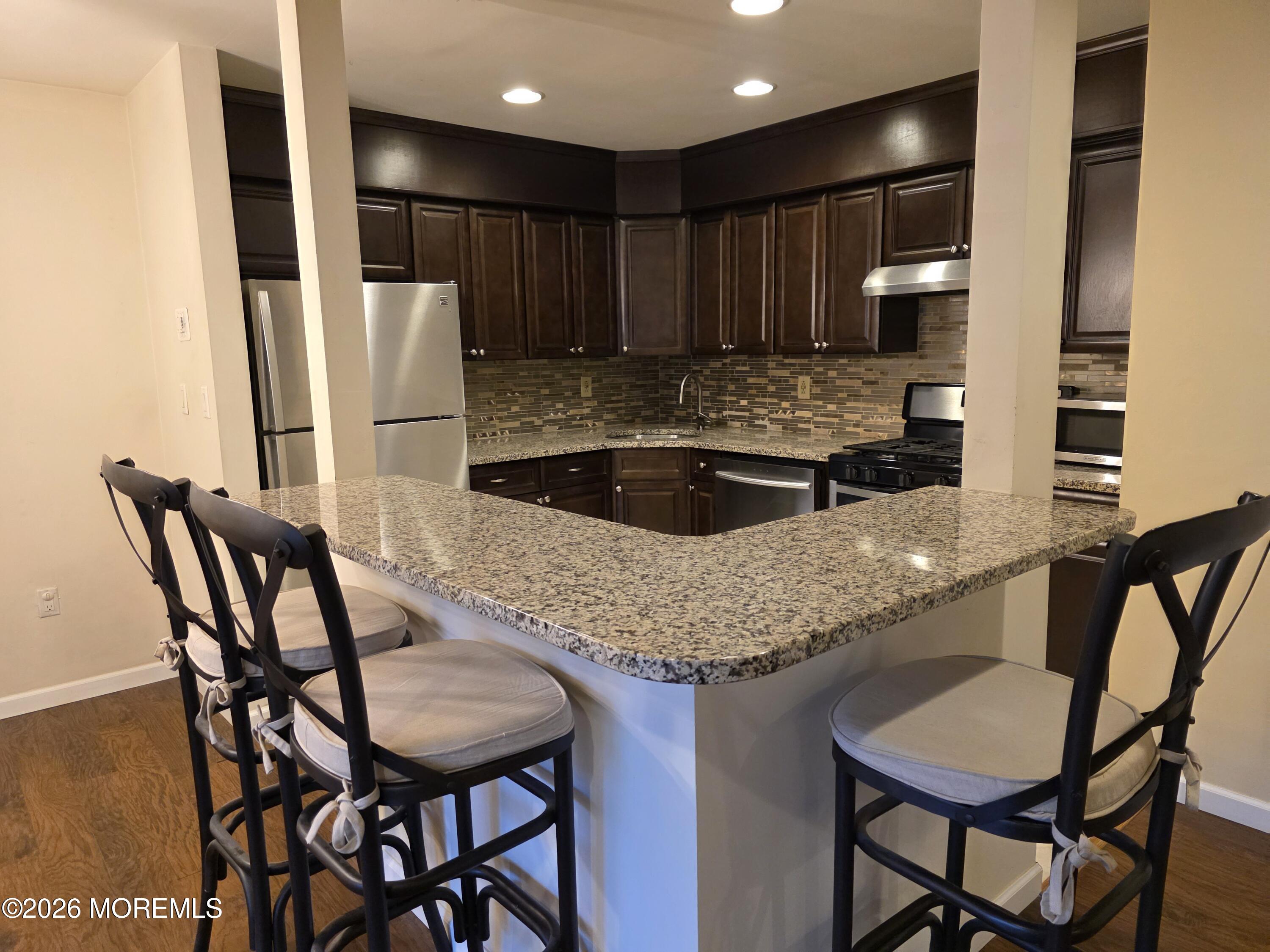 5 Claridge Court, Unit 4 Freehold, NJ 07728 - Photo 6 of 13 a kitchen with granite countertop a table chairs stove and refrigerator