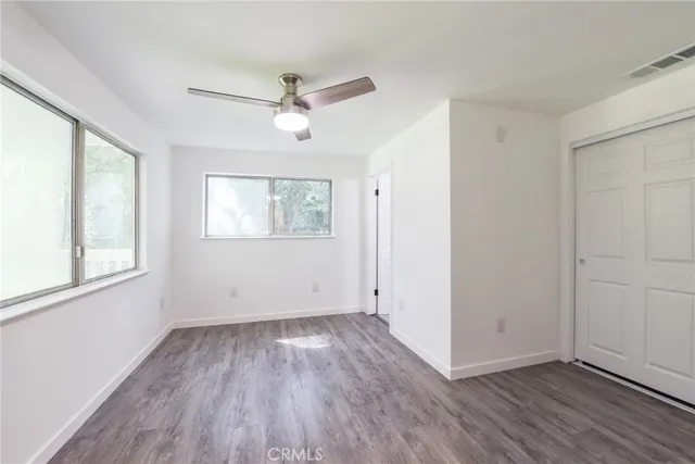 an empty room with wooden floor fan and windows