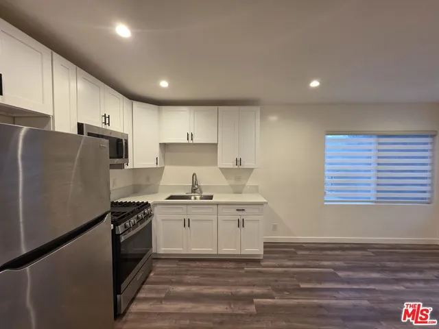 a kitchen with stainless steel appliances granite countertop a stove a refrigerator a sink dishwasher and white cabinets with wooden floor