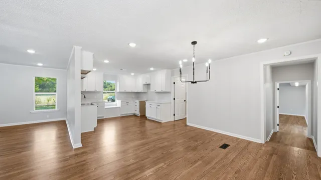 an empty room with wooden floor and kitchen view