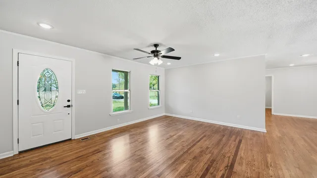 an empty room with wooden floor a ceiling fan and windows