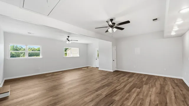 an empty room with wooden floor ceiling fan and windows