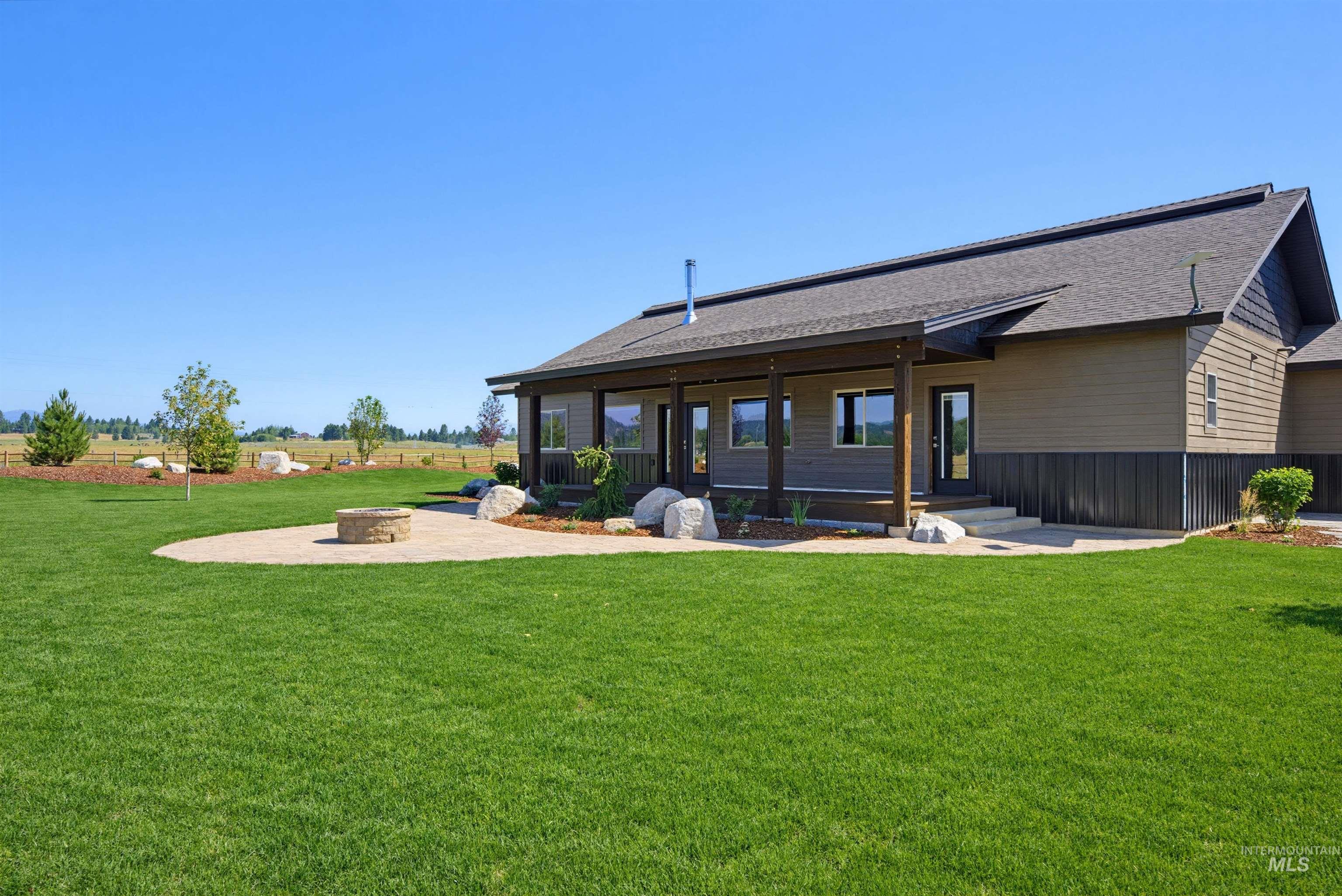 13945 Galloping Road McCall, ID 83638 - Photo 7 of 50 Expansive backyard featuring a stone fire pit on a circular patio, a covered porch with dark wood columns, and multiple windows