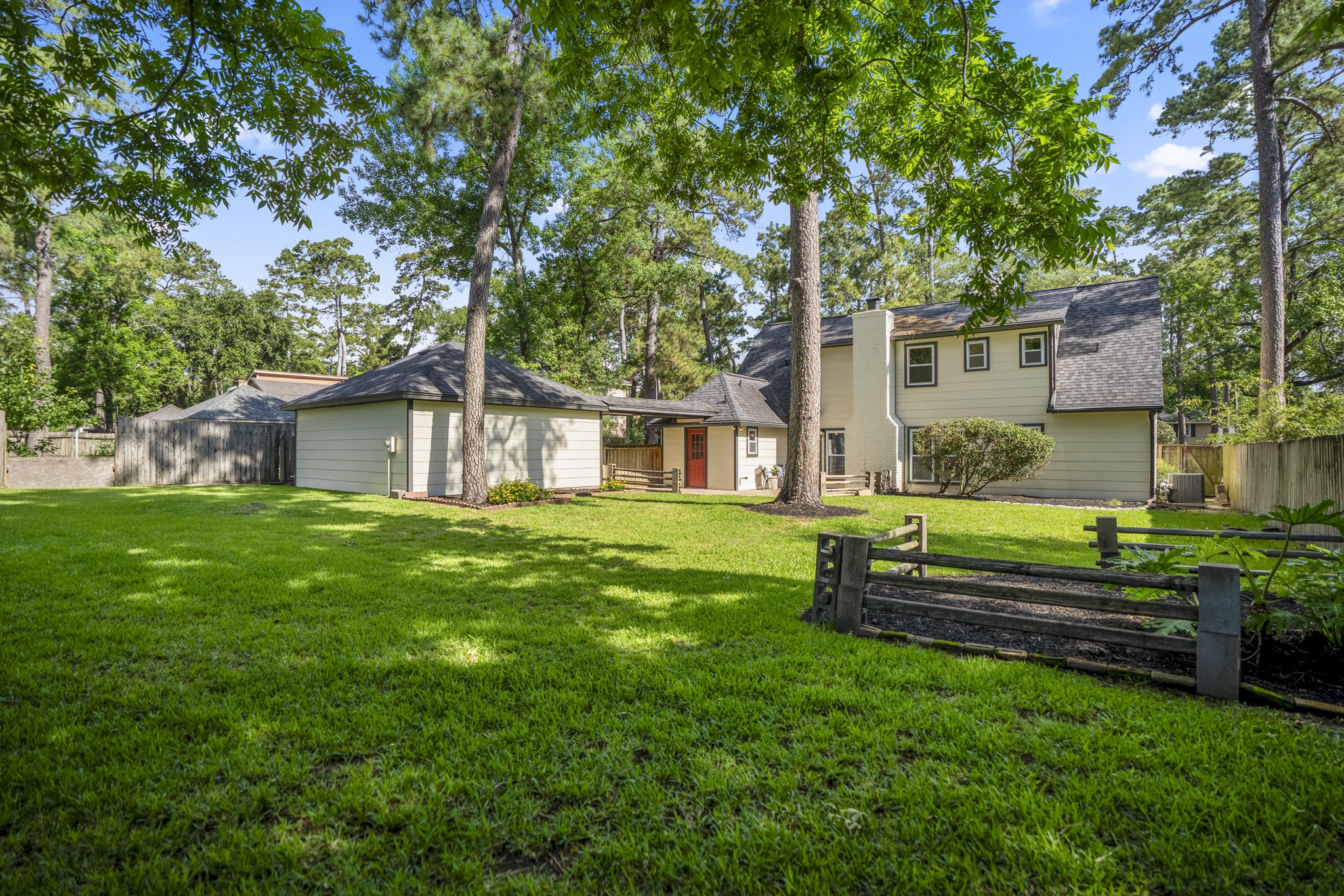 6303 Larkmount Drive Spring, TX 77389 - Photo 44 of 50 Stepping even farther back, the backyard starts to feel expansive with towering trees framing the lawn and open green space stretching between the home and fence line. The detached garage sits off to the side, while the refreshed exterior keeps the whole property feeling clean, cared for, and ready to enjoy.