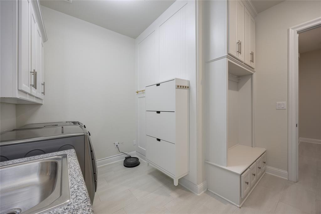 918 Sydney Lane Allen, TX 75013 - Photo 29 of 40 This laundry area features a stainless steel sink with a granite countertop, white cabinetry, and built-in storage with drawers and shelving