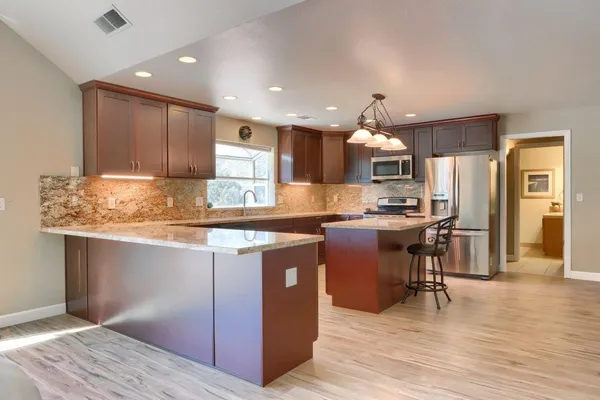 a kitchen with kitchen island granite countertop wooden floors stainless steel appliances and a counter