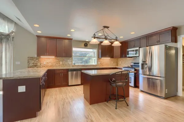 a kitchen with kitchen island granite countertop wooden floors stainless steel appliances and a counter