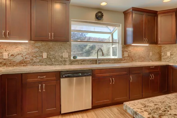 a sink with granite countertop cabinets and window