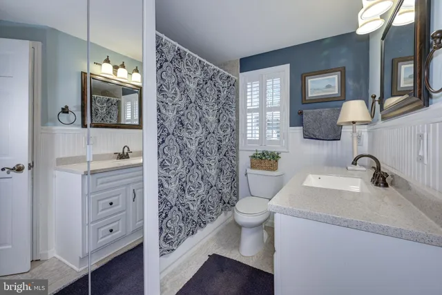 a bathroom with a granite countertop toilet a sink a mirror a window and vanity