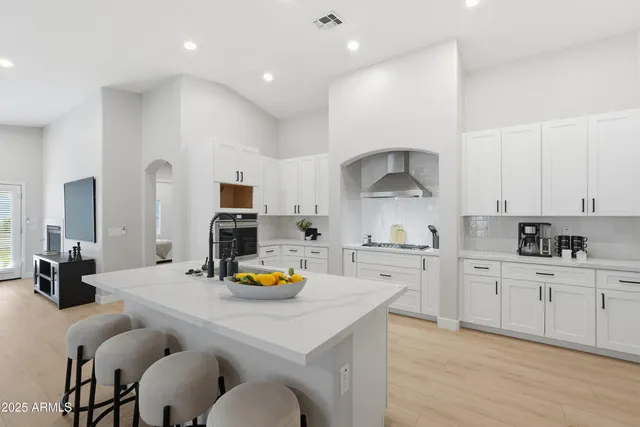 a kitchen with a sink a stove and chairs with white cabinets