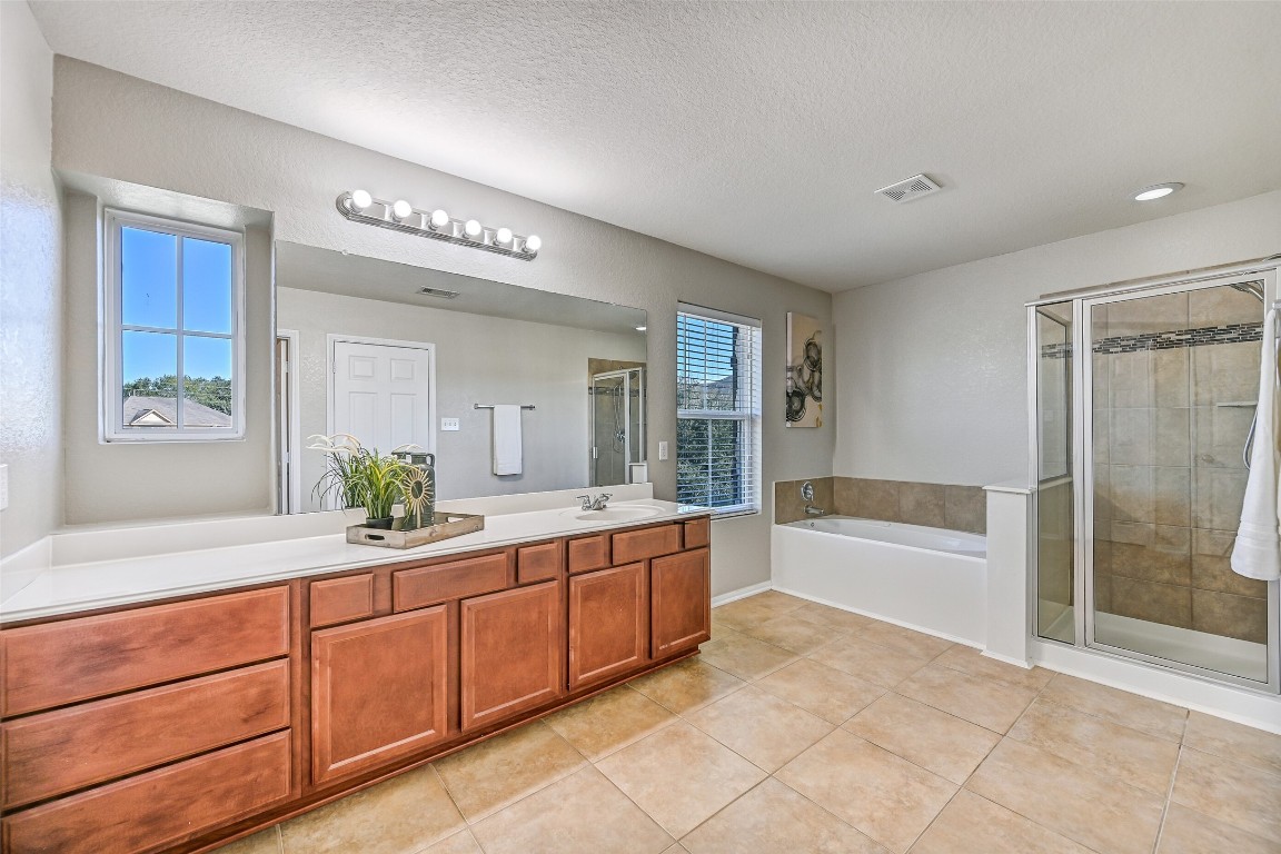 4206 Brightridge Court Rosenberg, TX 77471 - Photo 24 of 27 Relaxation awaits in this primary bathroom with a lengthy cultured marble vanity, a large mirror, Hollywood lighting, tile floors, an oversized soaking tub, and a separate glass-enclosed shower with a tile surround.