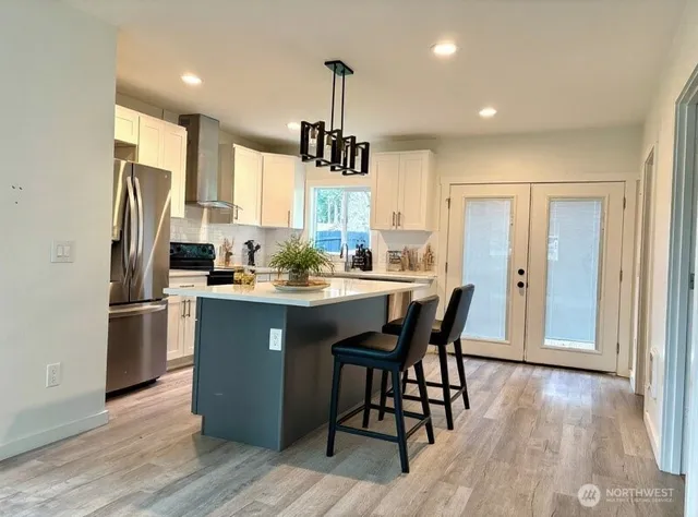 a kitchen with stainless steel appliances granite countertop a refrigerator a sink dishwasher a stove and white countertops with wooden floor