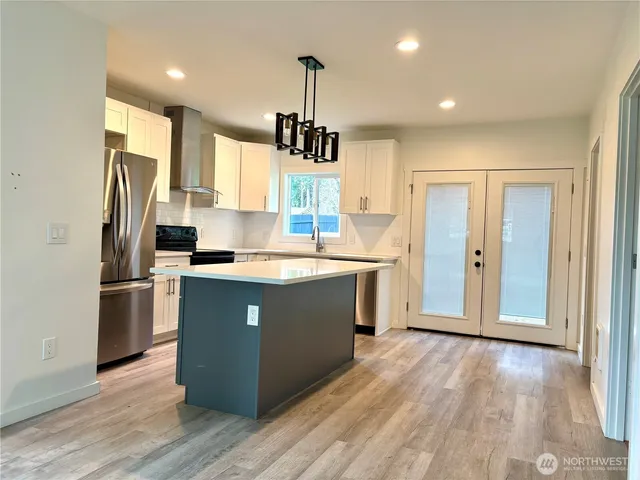 a kitchen with stainless steel appliances granite countertop a refrigerator a sink dishwasher a stove and white countertops with wooden floor