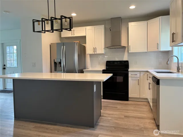 a kitchen with kitchen island granite countertop a refrigerator a sink dishwasher a stove and white cabinets with wooden floor