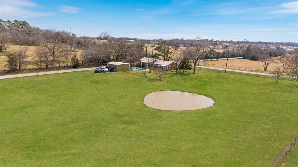 9213 Wilson Road Pilot Point, TX 76258 - Photo 4 of 36 Expansive green acreage featuring a natural pond, a single-story residence with a covered patio, and a detached outbuilding