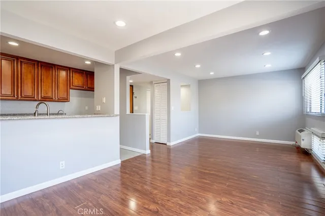 a view of empty room with wooden floor and kitchen