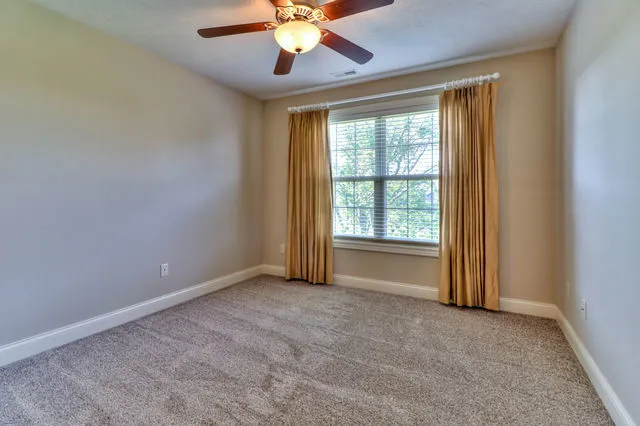 an empty room with chandelier fan and windows