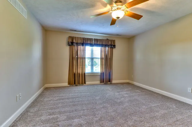 a view of an empty room with window and chandelier fan